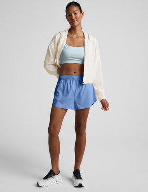 Woman wearing a light blue sports bra and shorts on a plain background. 