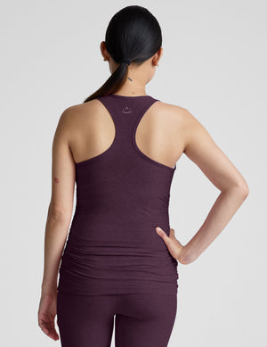 Woman wearing a purple maternity tank top and leggings on a light gray background. 