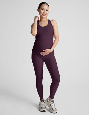 Woman wearing a purple maternity tank top and leggings on a light gray background. 