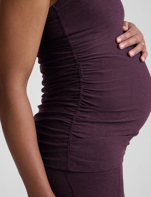 model wearing a purple maternity racerback tank top and leggings against a gray background. 