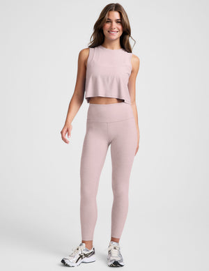 woman wearing a pink sleeveless cropped top and leggings against a plain background. 