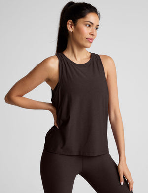 model wearing a brown sleeveless scoop neck top and leggings on a plain background. 