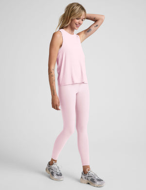 Woman wearing a light pink sleeveless top and leggings on a plain background. 