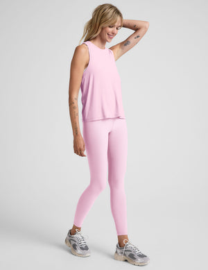 Woman wearing a pink relaxed fit sleeveless top and leggings on a light background. 