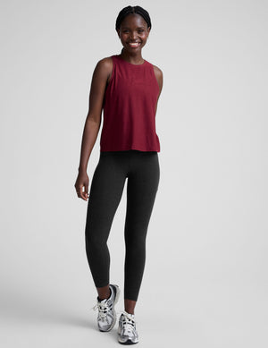 Woman wearing a red sleeveless top and black leggings against a plain background. 