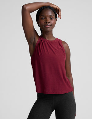 Woman wearing a red sleeveless top and black leggings against a plain background. 