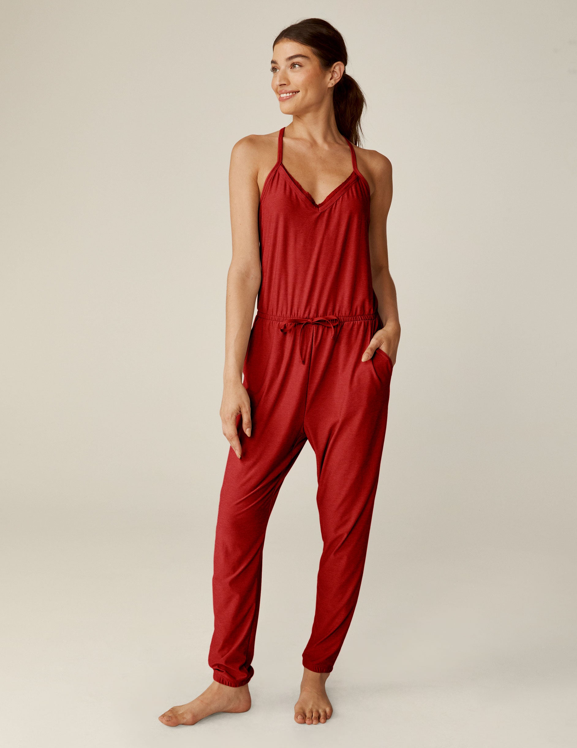 red racerback jogger jumpsuit with scalloped lace detailing on the neckline and a drawstring at waist. 