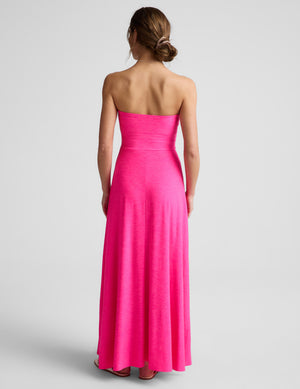Woman wearing a strapless pink strapless maxi dress on a light gray background. 