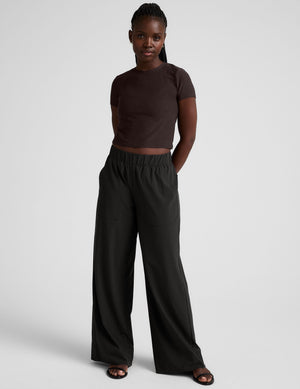 model wearing a brown crop top and black pants against a plain background. 