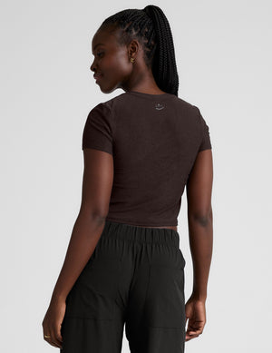 model wearing a brown crop top and black pants against a plain background. 