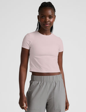 woman wearing a light pink crop top and gray pants on a white background. 