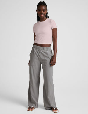 woman wearing a light pink crop top and gray pants on a white background. 