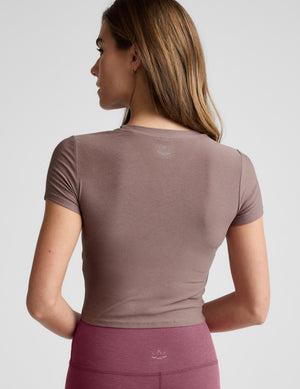 Woman wearing a brown cropped t-shirt and pink leggings against a plain background. 