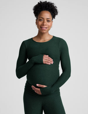 model wearing a green long-sleeve maternity top and leggings against a plain background. 