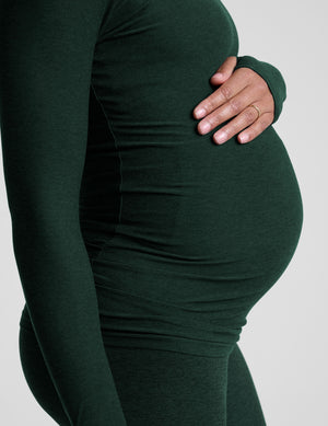 model wearing a green long-sleeve maternity top and leggings against a plain background. 