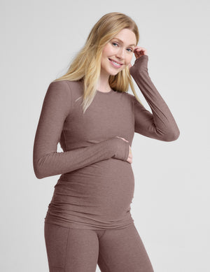 Woman wearing a brown maternity long-sleeve top and leggings against a light gray background. 