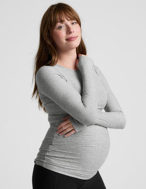 Pregnant woman wearing a gray long-sleeve top against a white background. 