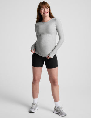Pregnant woman wearing a gray long-sleeve top against a white background. 