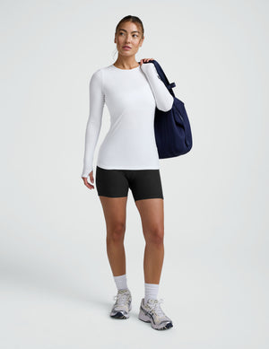 Woman wearing a long sleeve crew neck top and black biker shorts against a plain background. 