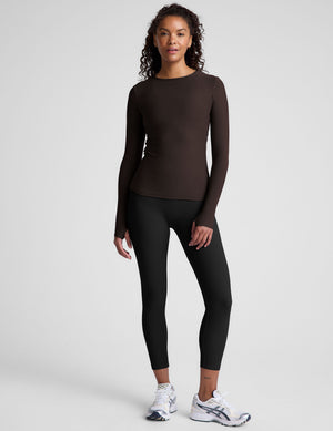 Woman wearing a brown long-sleeve top and black leggings on a plain background. 