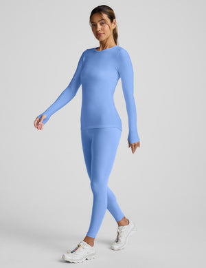 Woman wearing a blue long-sleeve top and leggings against a light gray background. 