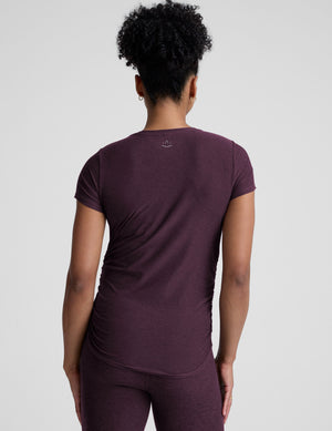 model wearing a purple maternity t-shirt and leggings against a light gray background. 
