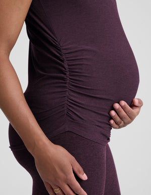 model wearing a purple maternity t-shirt and leggings against a light gray background. 