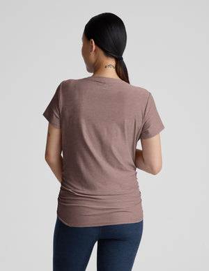 Pregnant woman wearing a brown shirt and blue leggings against a plain background. 