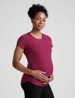 Woman wearing a magenta maternity t-shirt and black leggings against a plain background. 