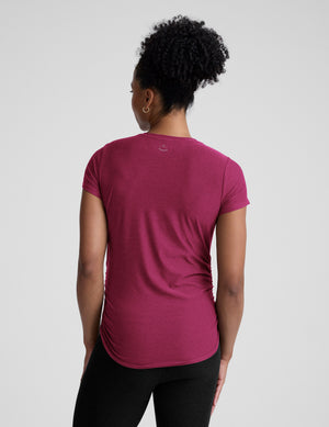 Woman wearing a magenta maternity t-shirt and black leggings against a plain background. 