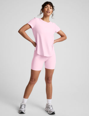 Woman wearing a pink crew neck t-shirt and pink biker shorts on a light gray background. 