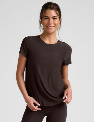woman wearing a brown t-shirt and leggings on a light gray background. 