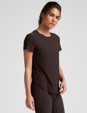 woman wearing a brown t-shirt and leggings on a light gray background. 