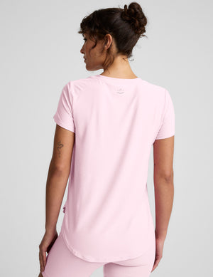 Woman wearing a pink short sleeve top and biker shorts on a light gray background. 