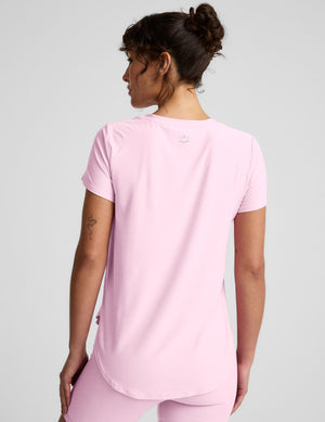 Woman wearing a pink crew neck t-shirt and pink biker shorts on a light gray background. 