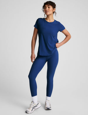 Woman wearing a blue crew neck t-shirt and leggings on a light gray background. 