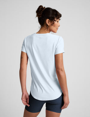 Woman wearing a light blue t-shirt and navy bike shorts on a plain background. 