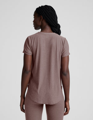 Woman wearing a brown t-shirt and leggings on a plain background. 