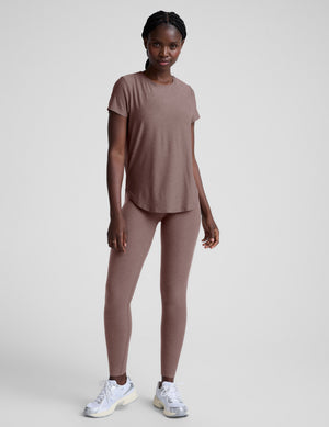 Woman wearing a brown t-shirt and leggings on a plain background. 