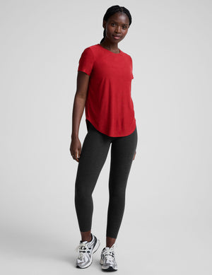 woman wearing a red t-shirt and dark pants on a light gray background. 