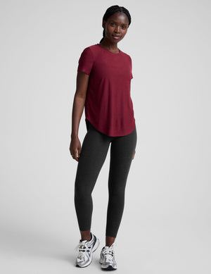 Woman wearing a red t-shirt and black leggings on a light gray background. 