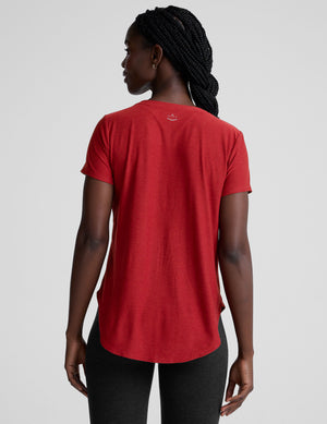 woman wearing a red t-shirt and dark pants on a light gray background. 