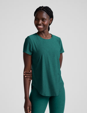 Woman wearing a green t-shirt and leggings against a plain background. 