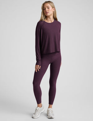 model wearing a purple scoop neck long-sleeve top and leggings on a light gray background. 