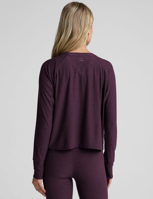 model wearing a purple scoop neck long-sleeve top and leggings on a light gray background. 