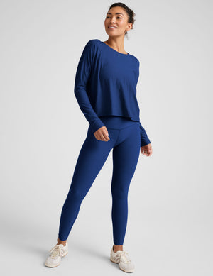 Woman wearing a blue long-sleeve top and leggings against a light background. 