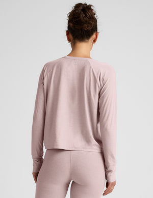 woman wearing a pink long-sleeve top and leggings on a plain background. 