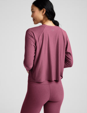 Woman wearing a purple long sleeve top and leggings against a light grey background. 