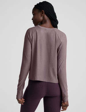 model wearing a light purple scoop neck long-sleeve top and purple leggings on a light gray background. 