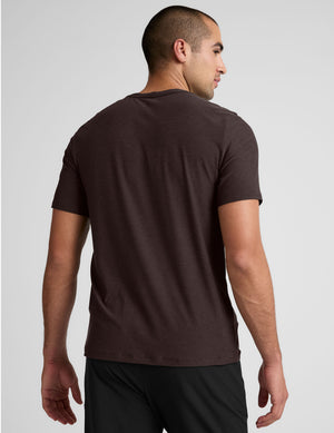 model wearing a brown men's short sleeve t-shirt against a gray background. 
